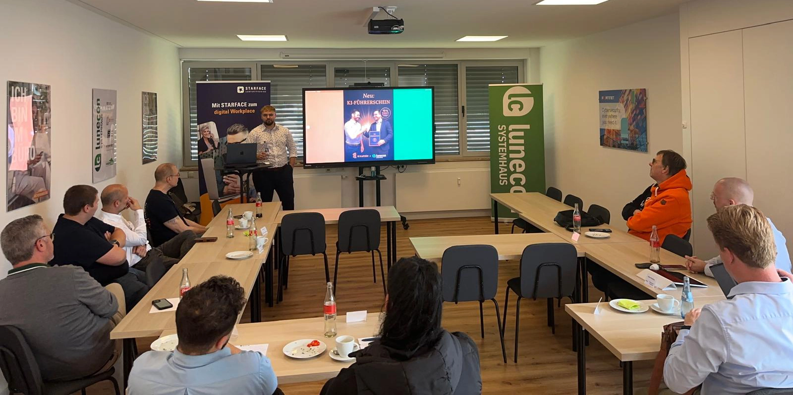 Ein Schulungsraum mit Teilnehmern, die einem Präsentator an einem Bildschirm zuhören.